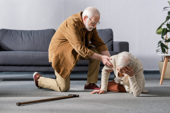 senior man helping wife lying on floor and touching head